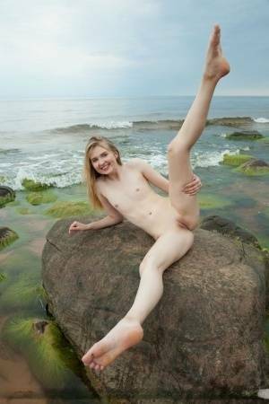 Slim teen Nimfa removes a black bikini to pose naked on seaside rocks on fangals.org