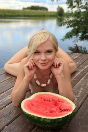 Beautiful blonde Feeona eats a watermelon while posing naked on lakeside dock on fangals.org